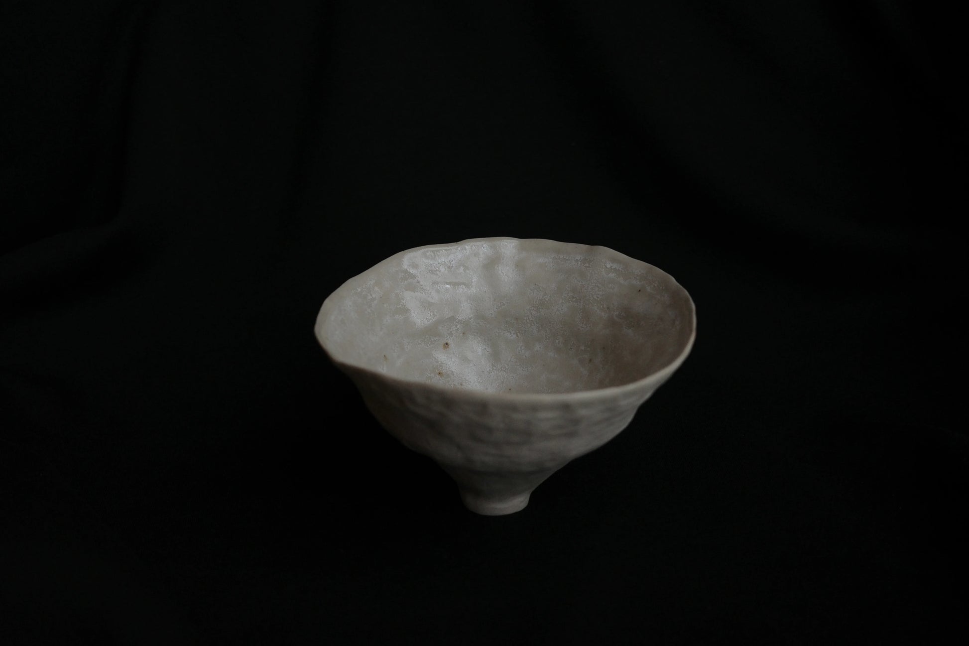 Handcrafted white ceramic bowl with organic texture on a dark background