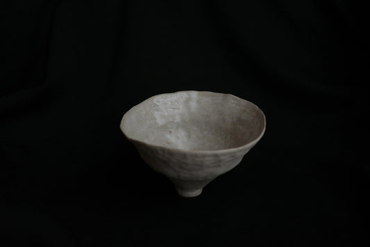 Handcrafted white ceramic bowl with organic texture on a dark background