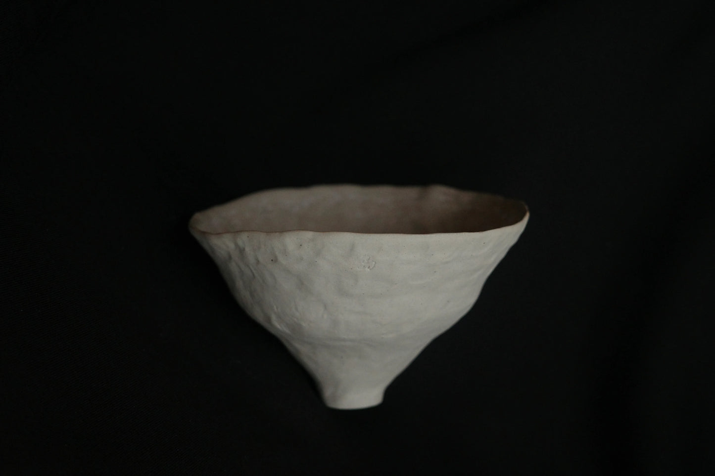 Handcrafted minimalist ceramic bowl with textured surface on black background