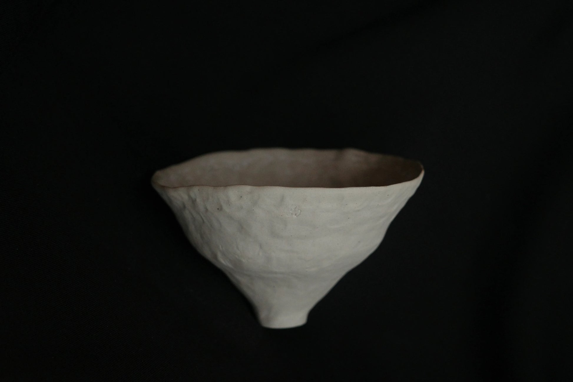 Handcrafted minimalist ceramic bowl with textured surface on black background