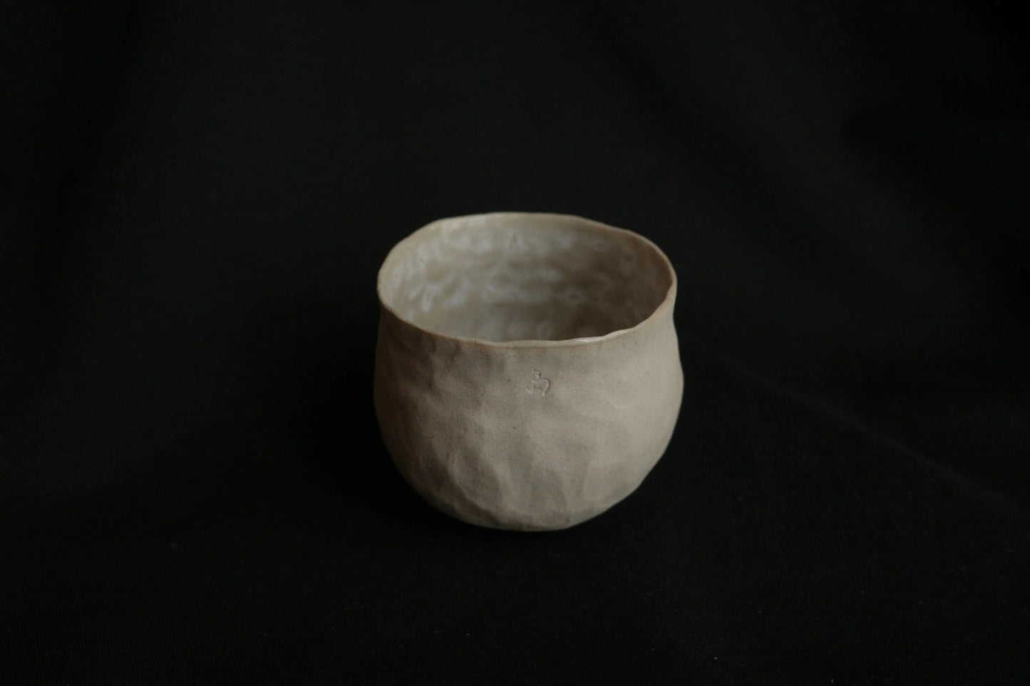 Handcrafted minimalist ceramic cup with textured surface on a black background
