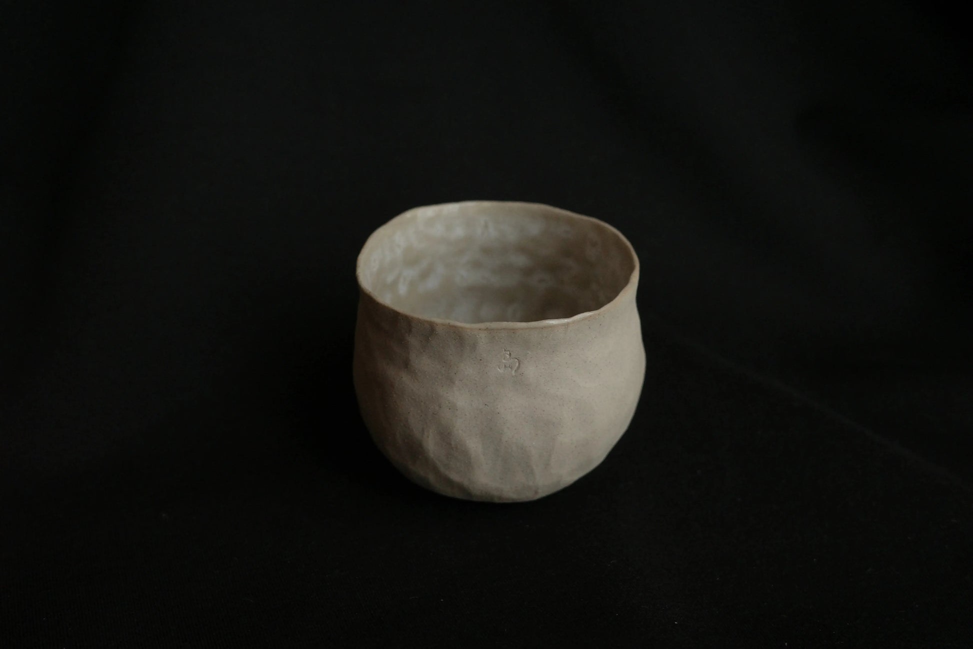 Handcrafted minimalist ceramic cup with textured surface on a black background