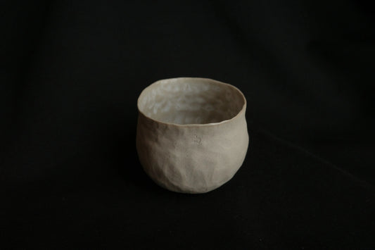 Handcrafted minimalist ceramic cup with textured surface on a black background