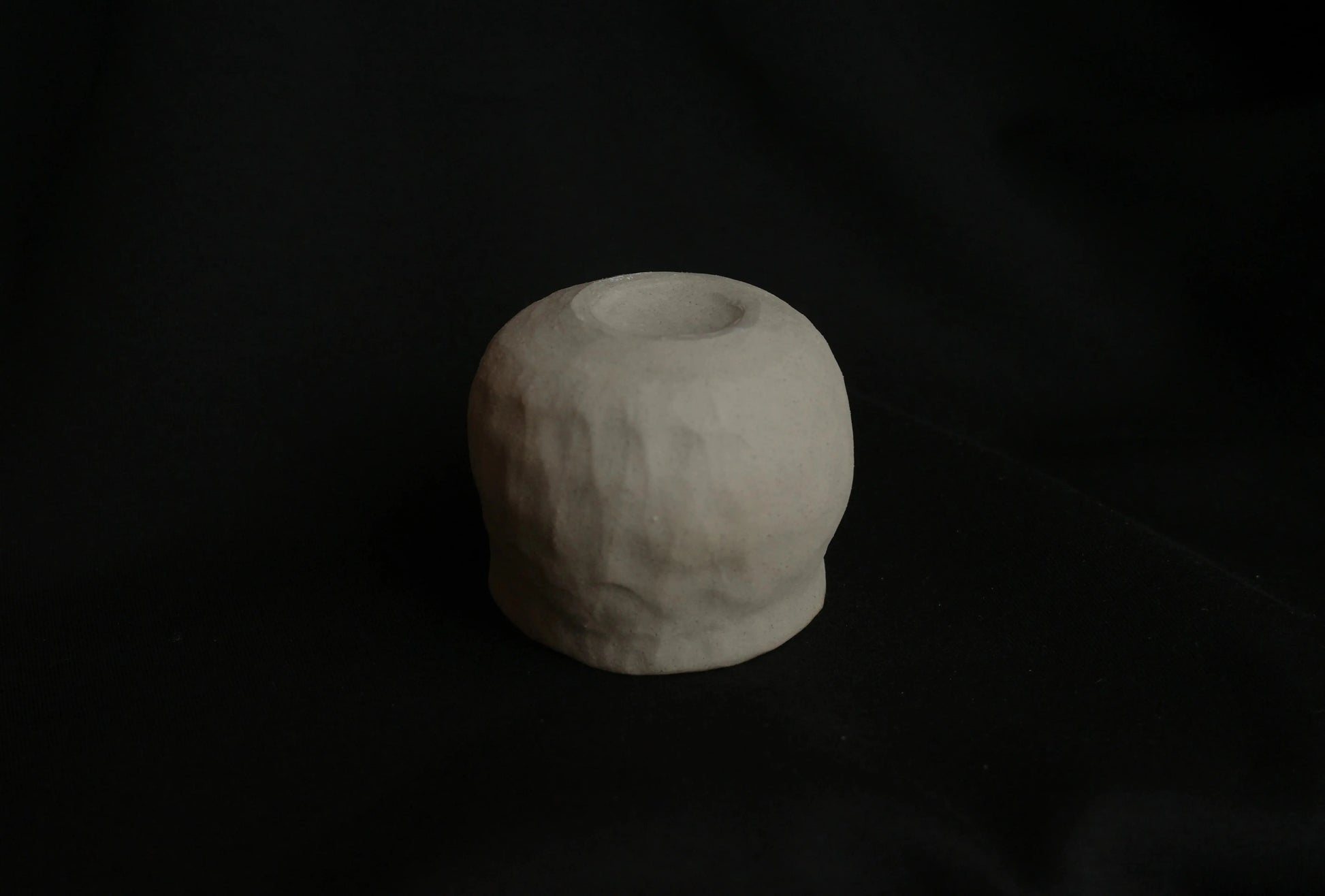 Minimalist handcrafted ceramic tealight holder with textured surface on black background